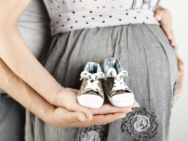 Pregnant couple holding baby shoes in the palm of their hands